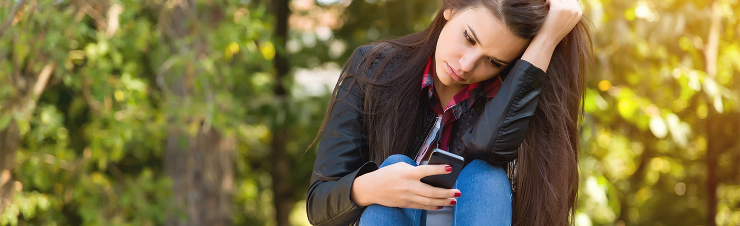 Mange opplever at private bilder blir spredt ulovlig på internett. Her er tipsene for å sikre bildene dine. Ung, trist jente på en benk med en mobiltelefon.