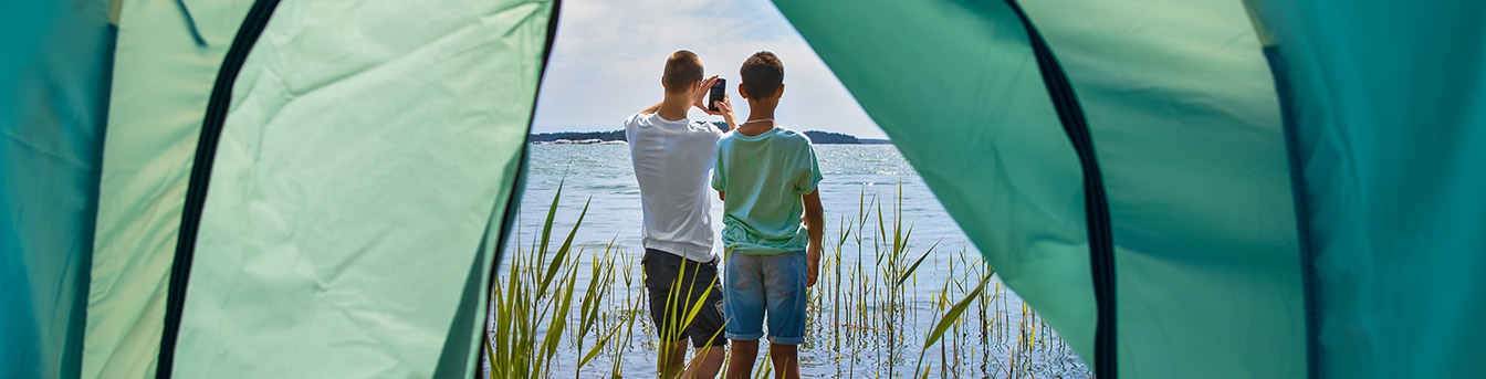 To gutter står utenfor et telt og ser på en mobil